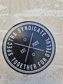 Black and white round sticker with the text "Spectra Syndicate Together For Otelul" written around a circle, and "Est. 2023" in the center.  The text is in a sans-serif font.