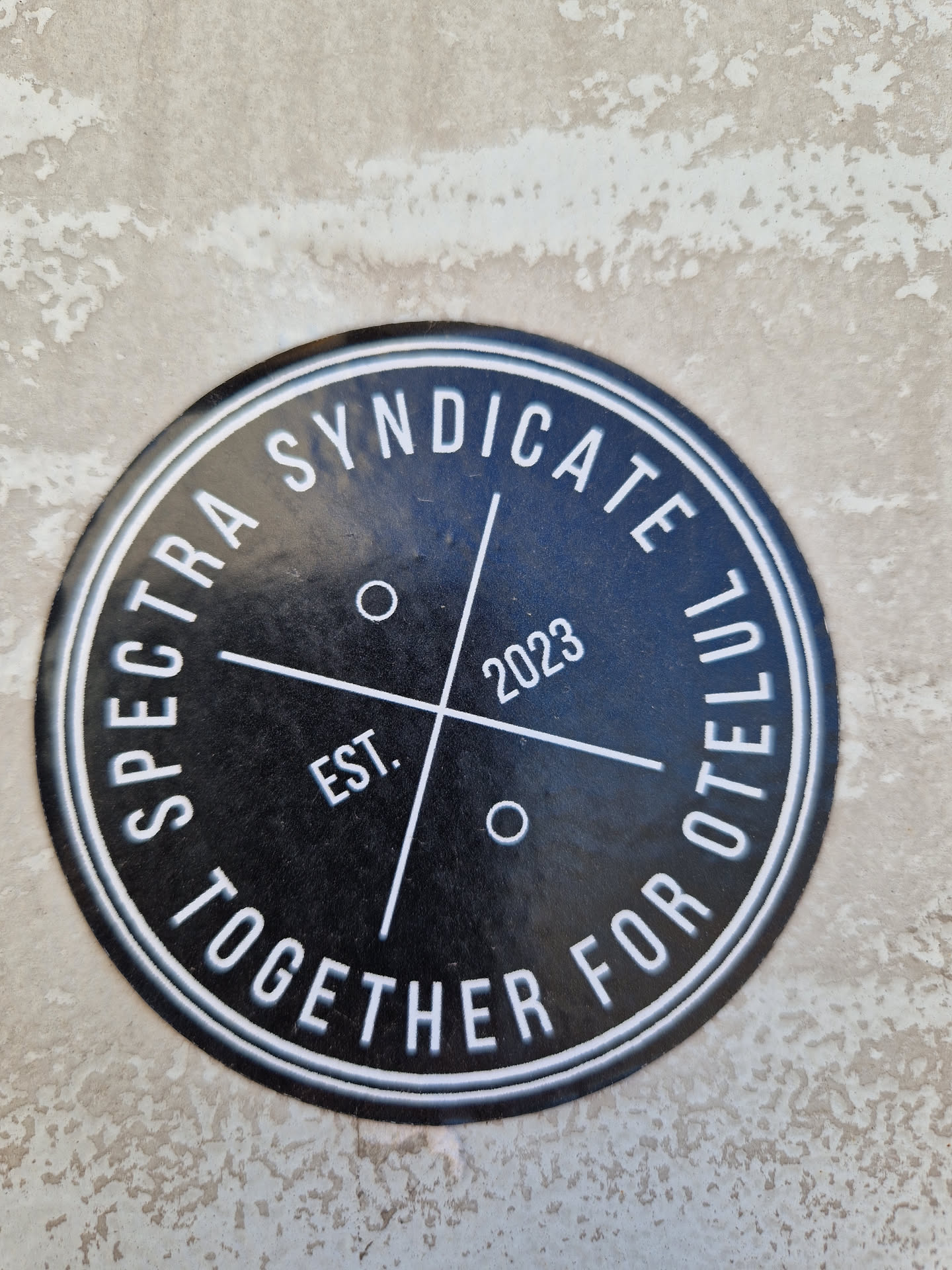 Black and white round sticker with the text "Spectra Syndicate Together For Otelul" written around a circle, and "Est. 2023" in the center.  The text is in a sans-serif font.