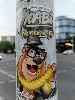Sticker featuring a cartoon illustration of a bear wearing a hat and glasses, with a gold rope around its neck and a tag with the number 21.  The sticker has the words "Moabit", "Anti- Rassismus jetzt", and "2er Gallery" on it.