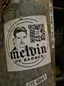 A sticker featuring a portrait of Melvin De Barber and a QR code. The design is in black and white with a circular border.