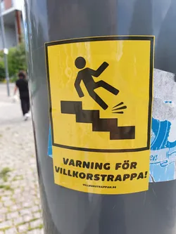 Yellow sticker with a pictogram of a person falling down the stairs and the text "VARNING FÖR VILLKORSTRAPPA!" which means "Warning for random stairs!" in Swedish.  There is also a website address at the bottom.
