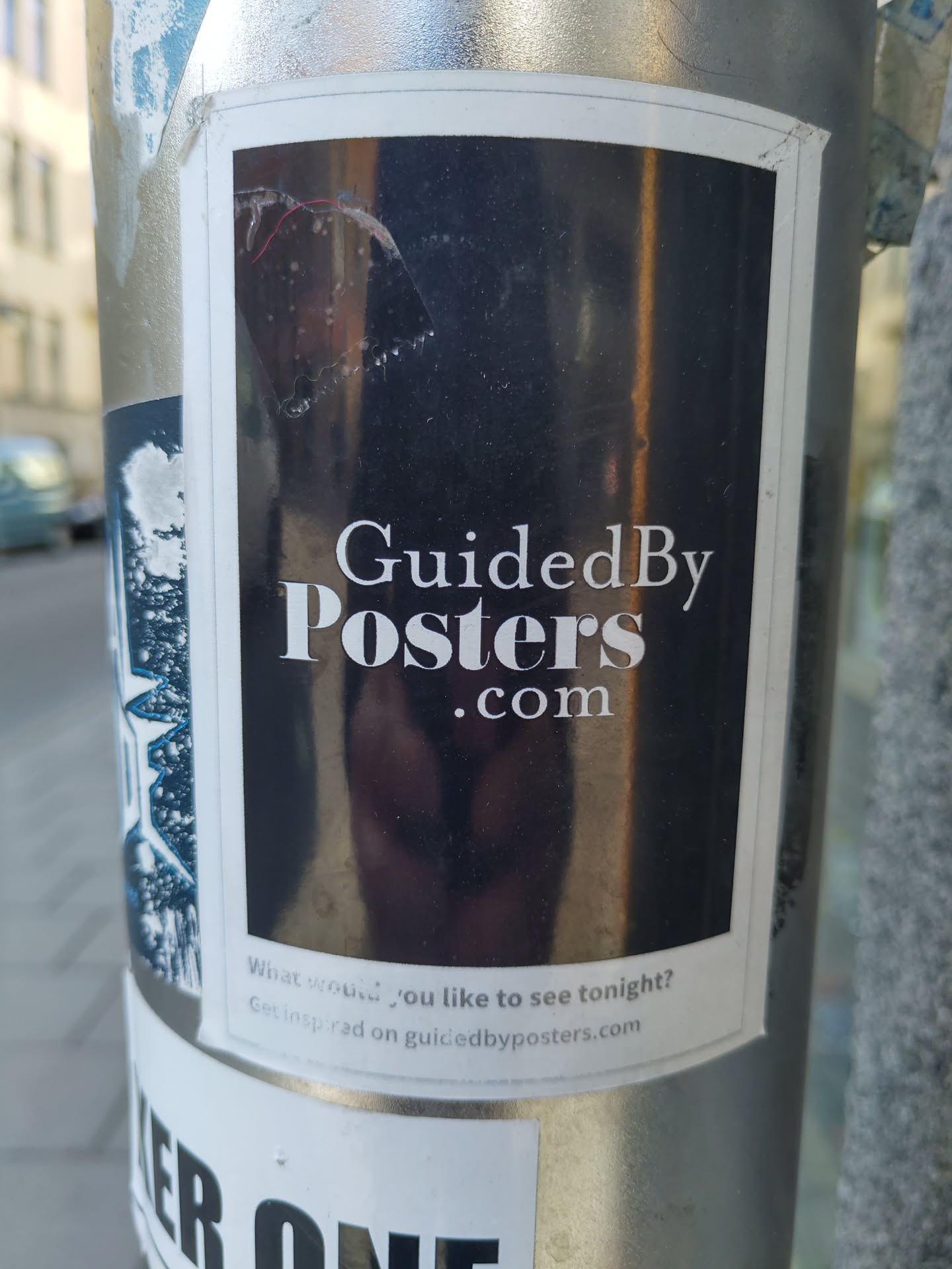 A sticker for Guided By Posters. The sticker has a dark background with the website name in white text.  Below is a small line of text that says, "What would you like to see tonight? Get inspired on guidedbyposters.com"