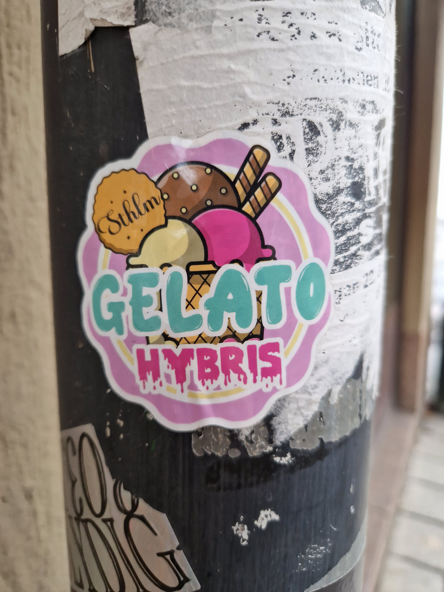 A sticker featuring an illustration of different gelato scoops in a waffle cone. The text 'Gelato Hybris' is prominently displayed. A small cookie with the word 'Sühlim' is also visible.