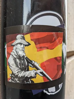 This sticker features a stylized illustration of a frontiersman with a rifle, set against a bold color scheme of red, yellow, and green. The image evokes a sense of the American frontier and pioneer history. The art style is graphic and slightly reminiscent of vintage posters or propaganda.