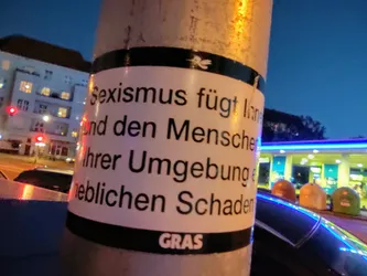 A sticker on a pole with text in German that translates to: "Sexism causes long-term damage and significant harm to people and their environment."