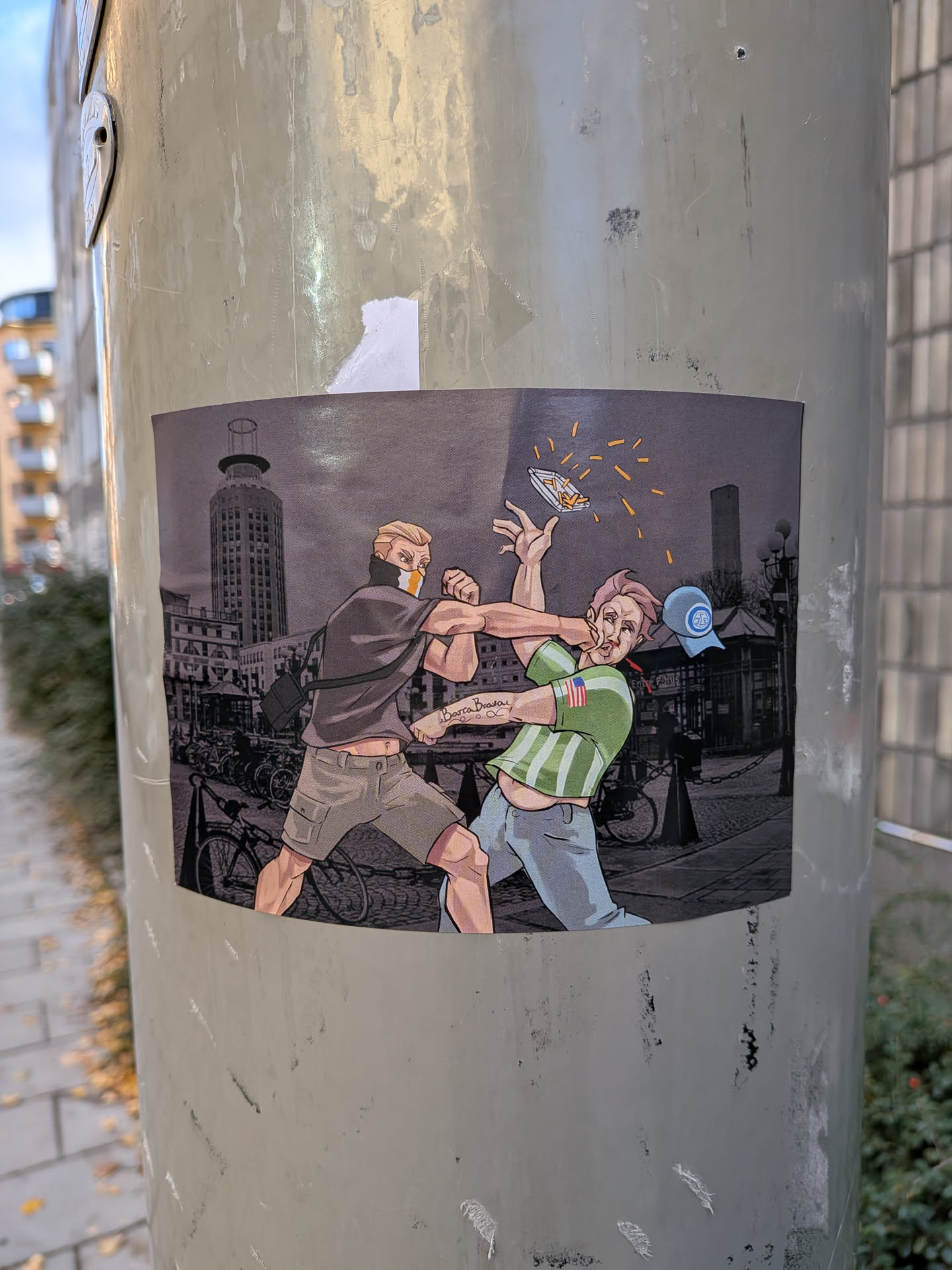 The sticker depicts a cartoonish scene of two men in a physical altercation. The man on the left, wearing a dark shirt and cargo shorts, is throwing a punch. He has a mask or bandana covering the lower half of his face with an orange and white pattern. The man on the right, wearing a green and white striped shirt and light blue pants, is recoiling from the punch, with his hat flying off his head. A tray of french fries is also airborne, scattering in the air. The background is a grayscale depiction of a city street with buildings, bicycles, and streetlights. The overall style is illustrative with bold outlines and vibrant colors for the characters and their actions, contrasting with the muted background.