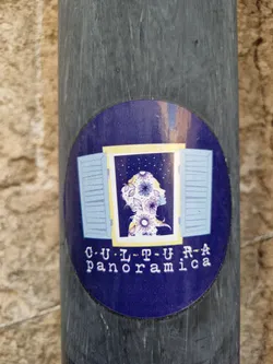 Round sticker with a dark blue background. It depicts a person's silhouette decorated with flowers, seen through a window with light blue shutters. The text "CULTURA Panoramica" is printed below the image.