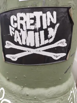 Street sticker Black and white sticker with the text "CRETIN FAMILY" in a stylized font, along with a graphic of crossed bones. The sticker is affixed to a green surface.