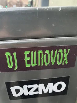 A pixel art style sticker featuring the text "DJ EUROVOX" in lime green on a dark background.  There is also a Dizmo sticker below it.