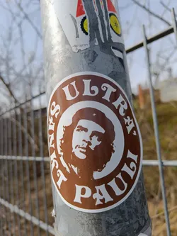 A brown and white circular sticker featuring a portrait of Che Guevara. The text "Ultras Pauli" is written around the image in a stylized font.