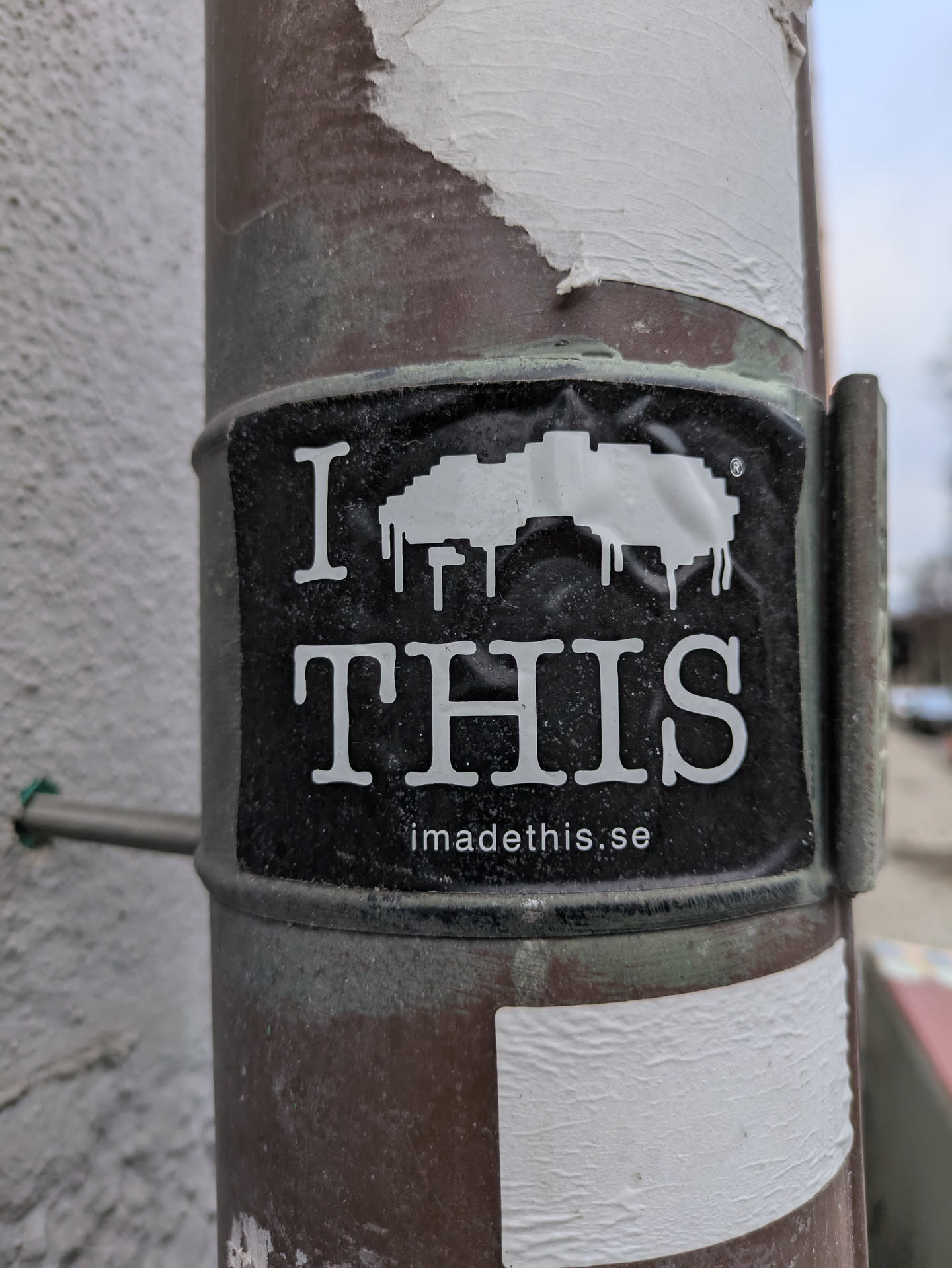 A black and white sticker with a simple design and text. The text on the sticker says \"I \u2764 THIS\" and has a website address at the bottom. The sticker is attached to a brown pole.