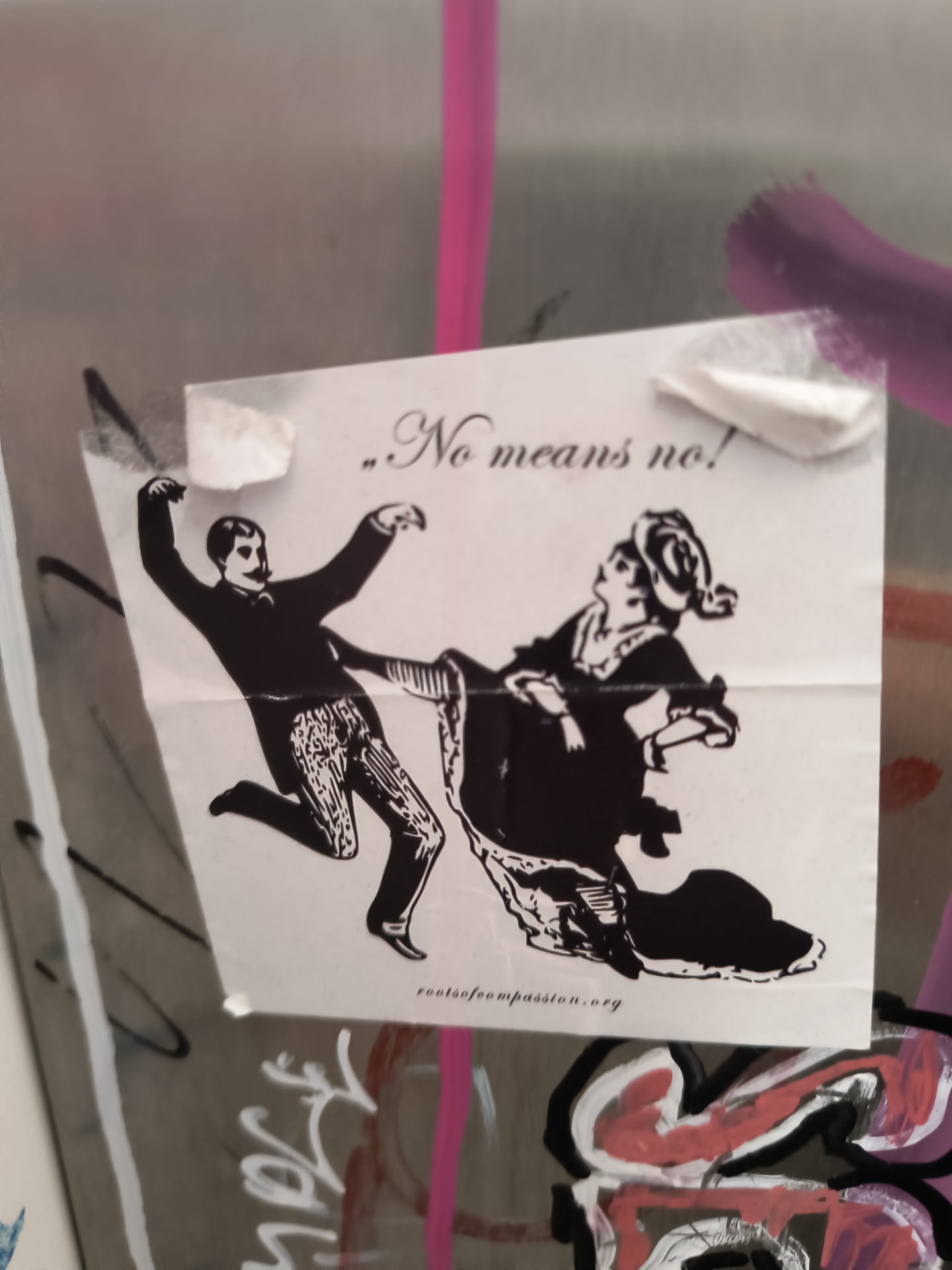 The sticker is printed on white paper with black ink. It features a vintage-style illustration depicting a man in a suit kicking or gesturing forcefully towards a woman who is dressed in historical attire and appears to be recoiling or resisting. The text '„No means no!' is prominently displayed in a stylized font above the figures. Below the illustration, the URL 'rootsofcompassion.org' is printed in smaller text. The sticker is attached with visible pieces of tape and is slightly creased.