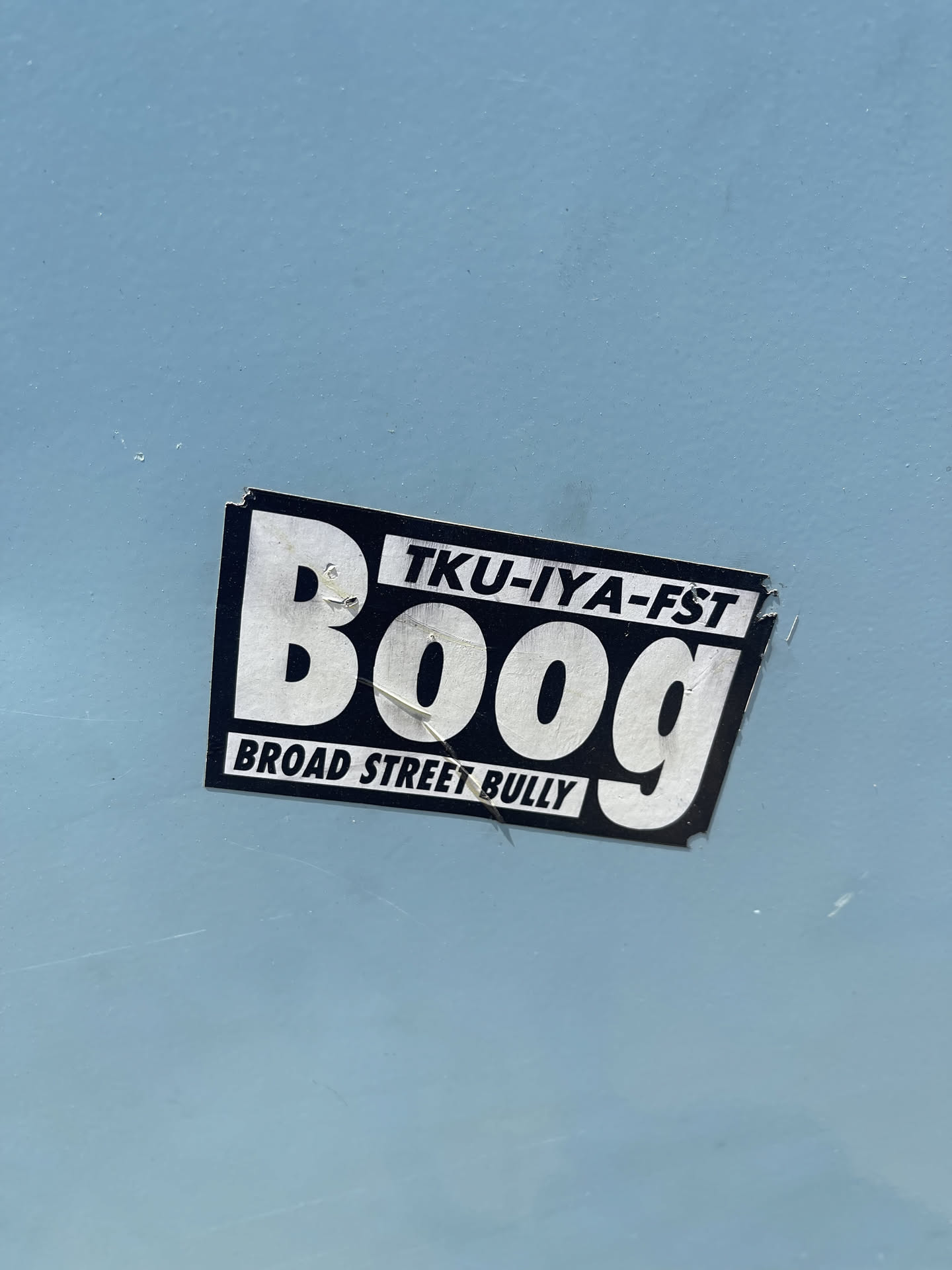 The sticker is rectangular with a black border and a white background. The word 'Boog' is prominently displayed in large, bold, white sans-serif letters. Above 'Boog', in smaller white text, is 'TKU-IYA-FST'. Below 'Boog', also in smaller white text, is 'BROAD STREET BULLY'. The sticker appears slightly worn and has a few small tears at the edges.