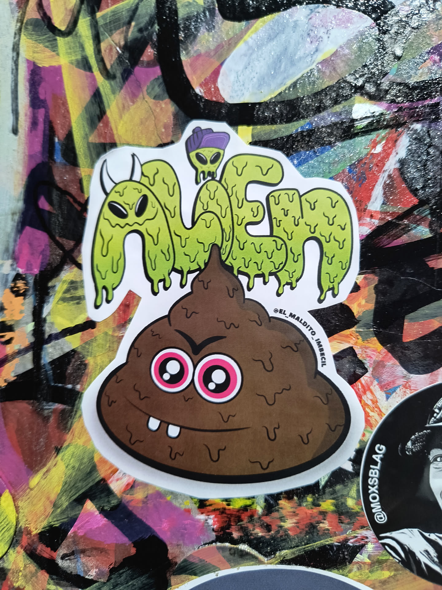 The sticker features two main elements stacked vertically. The top element is text that spells out 'ALIEN' in a dripping, slime-like font, colored light green. Each letter is outlined in black and has a white border. At the top of the 'A', there's a small, simplified green alien wearing a purple hat. The bottom element is a brown, stylized poop emoji with a mischievous grin, featuring two prominent teeth. Its eyes are large and round with bright pink irises and white pupils, giving it an angry or mischievous expression. It also has a white border and a black outline.