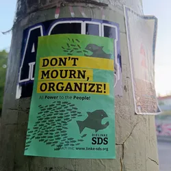 A green and yellow sticker with a graphic of fish forming a large fish, promoting the organization DIE LINKE SDS.  The sticker encourages viewers to organize rather than mourn, advocating for people's power. A website address is included for further engagement.