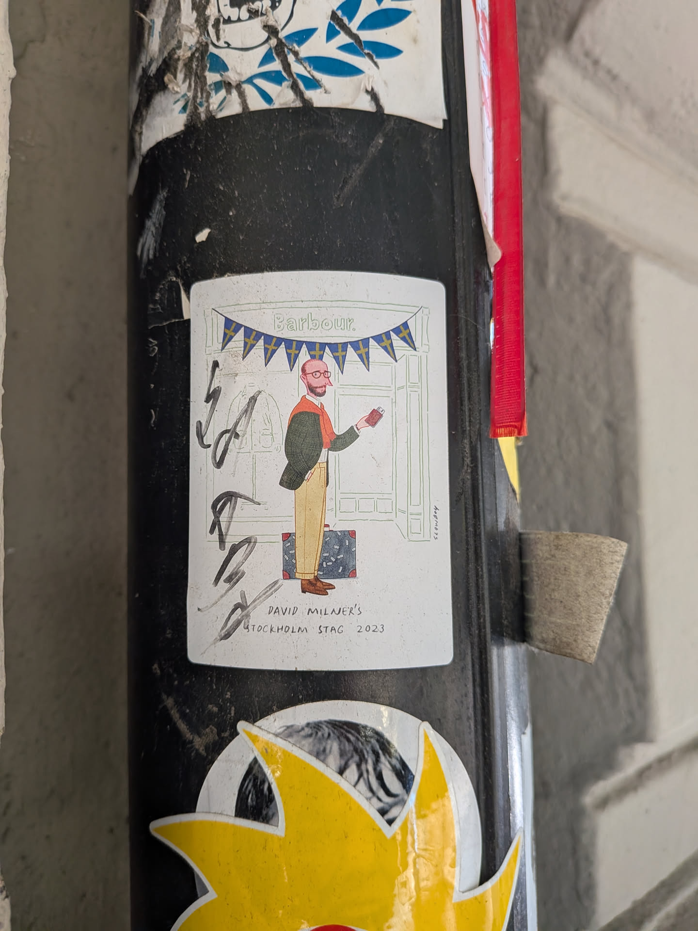 A vertical rectangular sticker with rounded corners featuring a menswear illustration by artist Slowboy. The drawing shows a bearded, bald man with round glasses dressed in a green tailored jacket, beige trousers, brown oxford shoes, and an orange sweater draped over his shoulders. He holds a small red passport in his hand, standing beside a patterned suitcase in front of a Barbour shop decorated with a string of Swedish flag bunting. Hand-drawn text at the bottom reads 'DAVID MILNER'S STOCKHOLM STAG 2023', and the artist's signature 'slowboy' appears vertically along the right. A black marker scribble partially obscures the left side of the sticker.