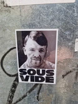 Black and white photo of a man with the word "Sous Vide" written below it. The sticker is placed on a textured wall.