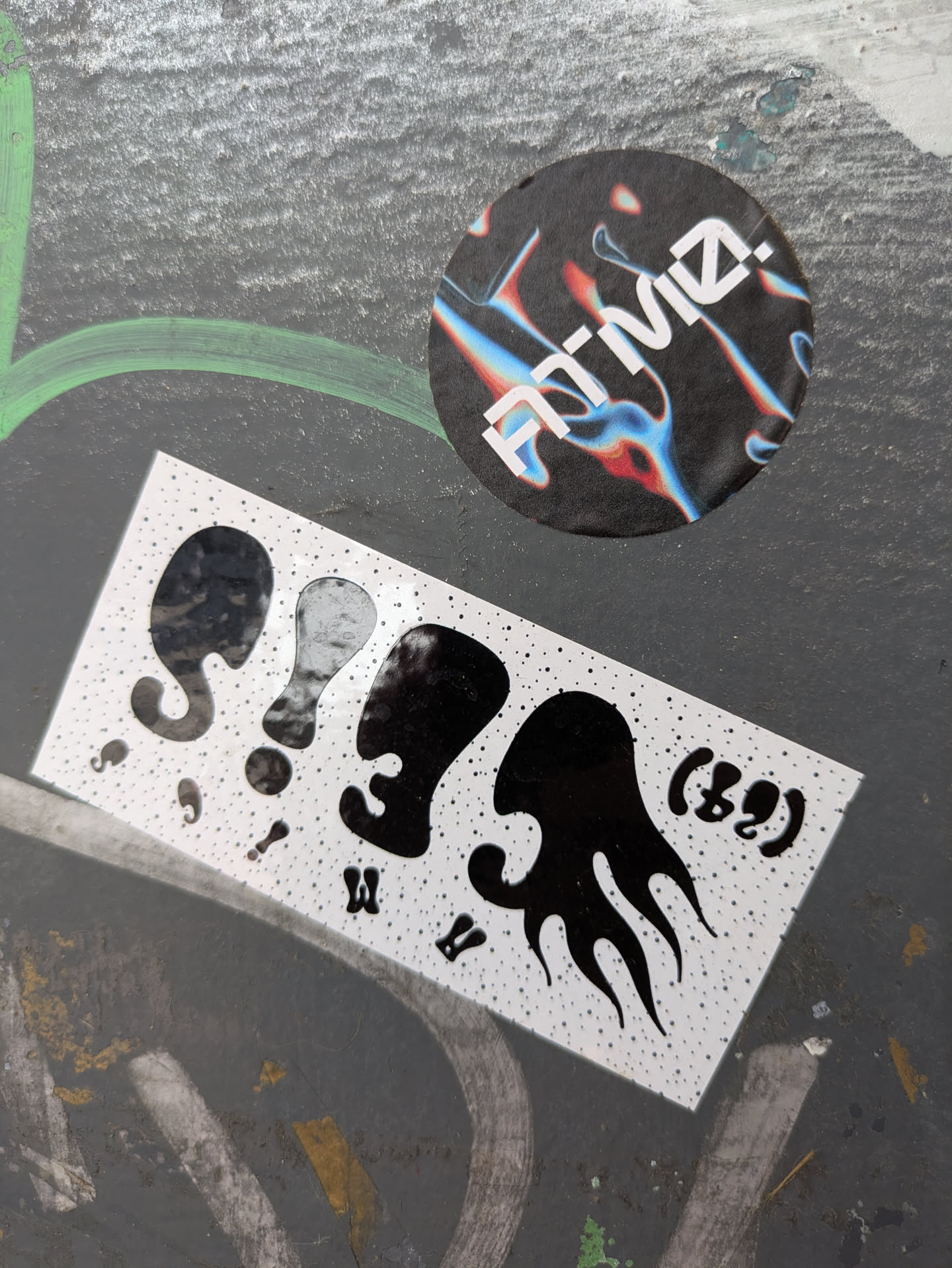 The sticker contains a series of stylized black shapes reminiscent of figures or objects, set against a backdrop of white dots. It has a playful and somewhat abstract design.