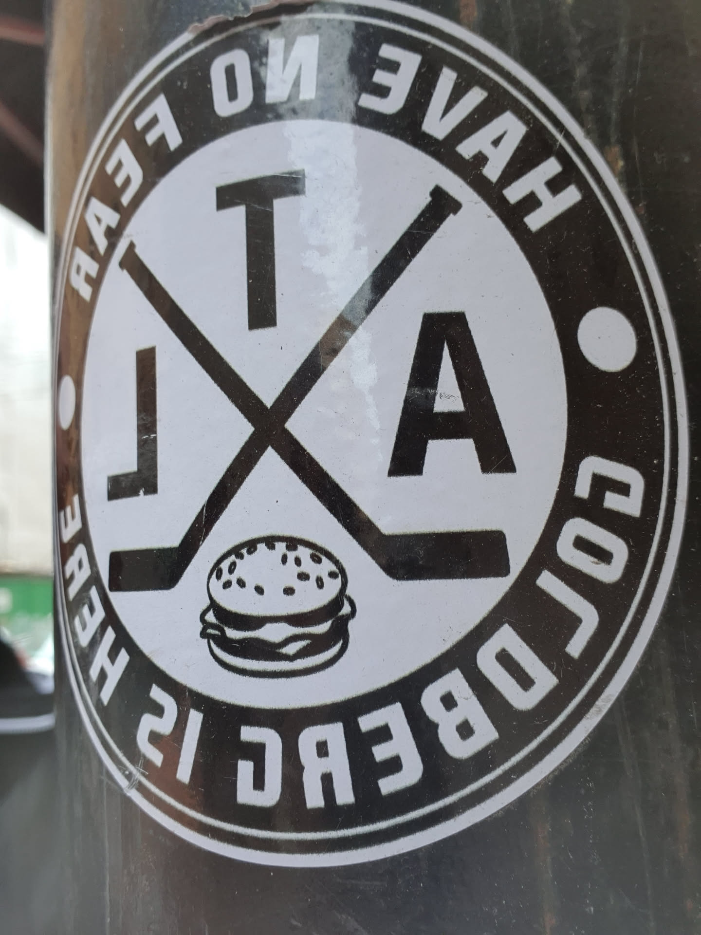 A black and white sticker with a logo. The logo includes crossed hockey sticks, the letters TA, a burger and the text "Goldberg is here. Have no fear."