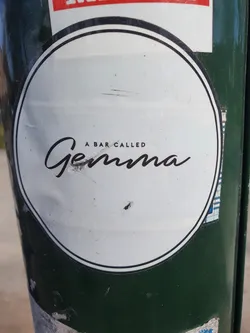 Round white sticker with black text on a green pole.  The text says "A bar called Gemma" in a stylized font.