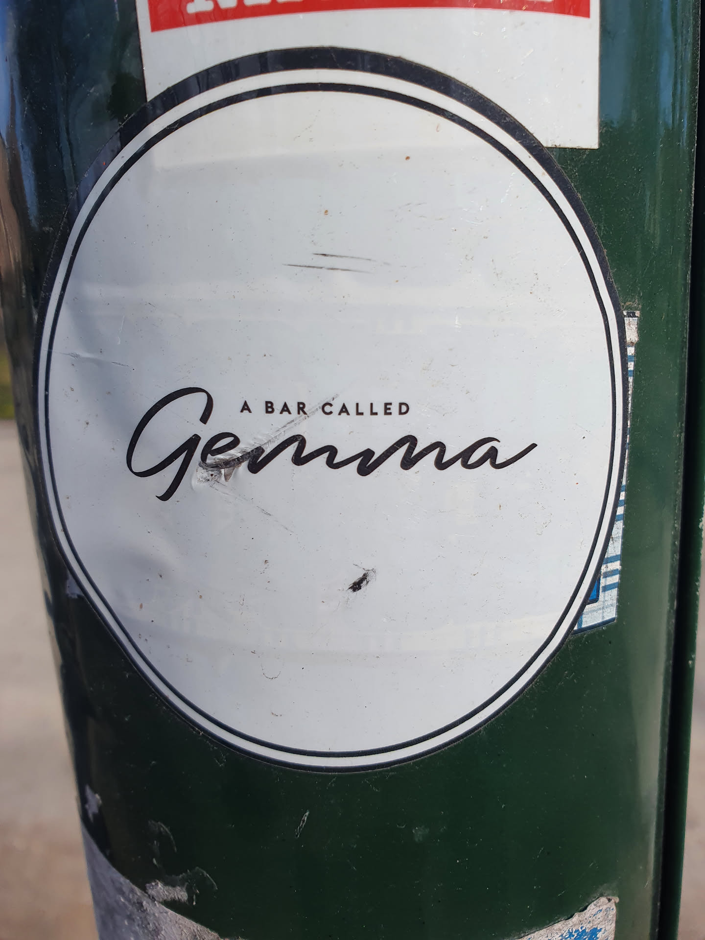 Round white sticker with black text on a green pole.  The text says "A bar called Gemma" in a stylized font.
