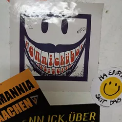 A square sticker featuring a large smiling face with exaggerated teeth. The text inside the teeth is in German. The style is reminiscent of vintage or psychedelic art.