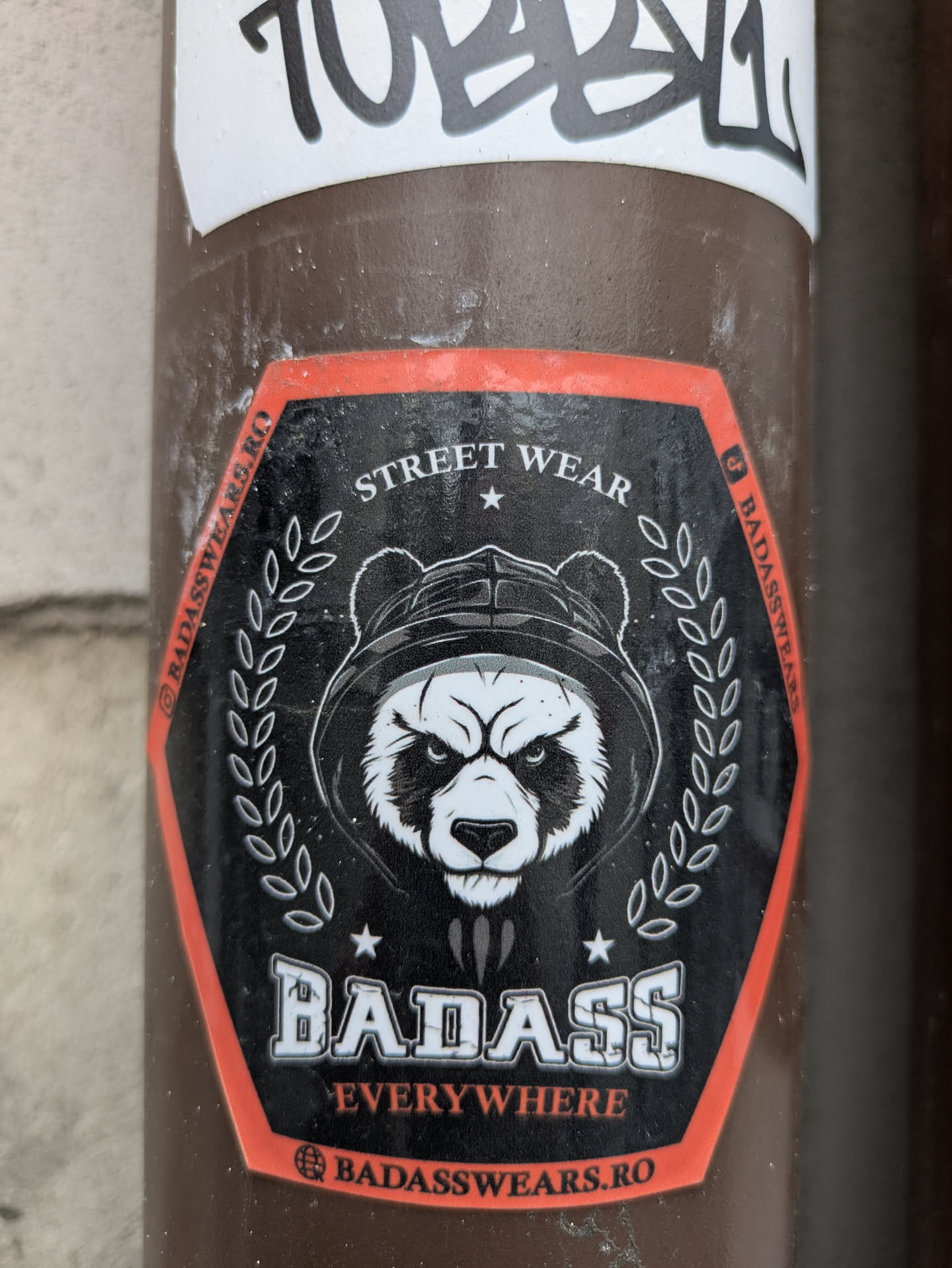 This sticker features a fierce panda wearing a hoodie, encircled by laurel leaves. The text "STREET WEAR" is at the top, and "BADASS EVERYWHERE" is at the bottom. The website badasswears.ro is also printed on the sticker. The sticker has a black background with red borders.