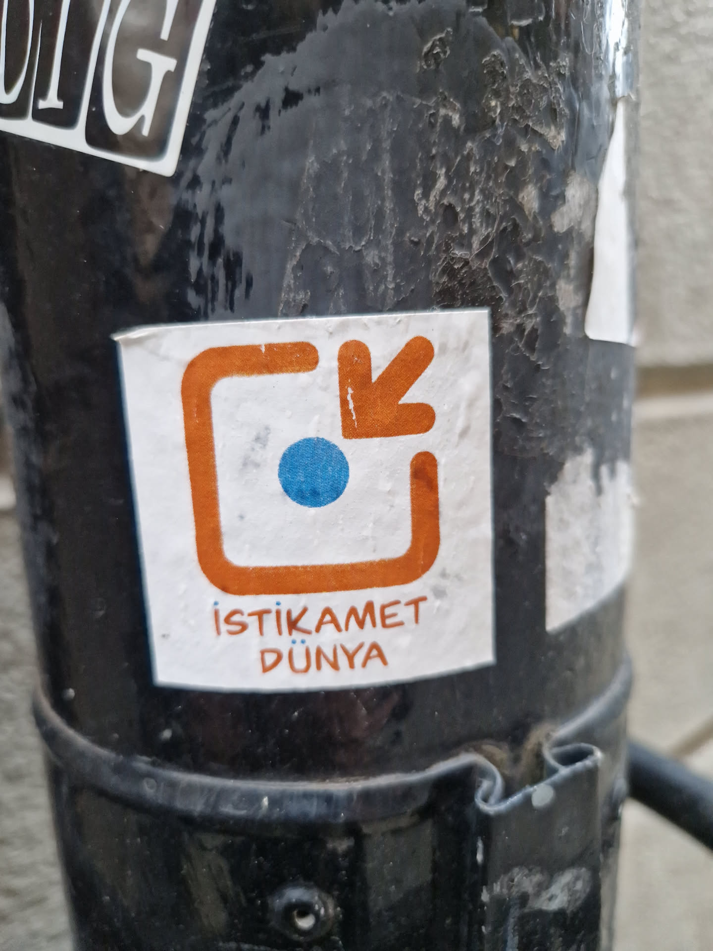 A sticker with an orange square and arrow pointing down, a blue dot inside. The text below says "İstikamet Dünya", which translates to "Direction World" in Turkish.