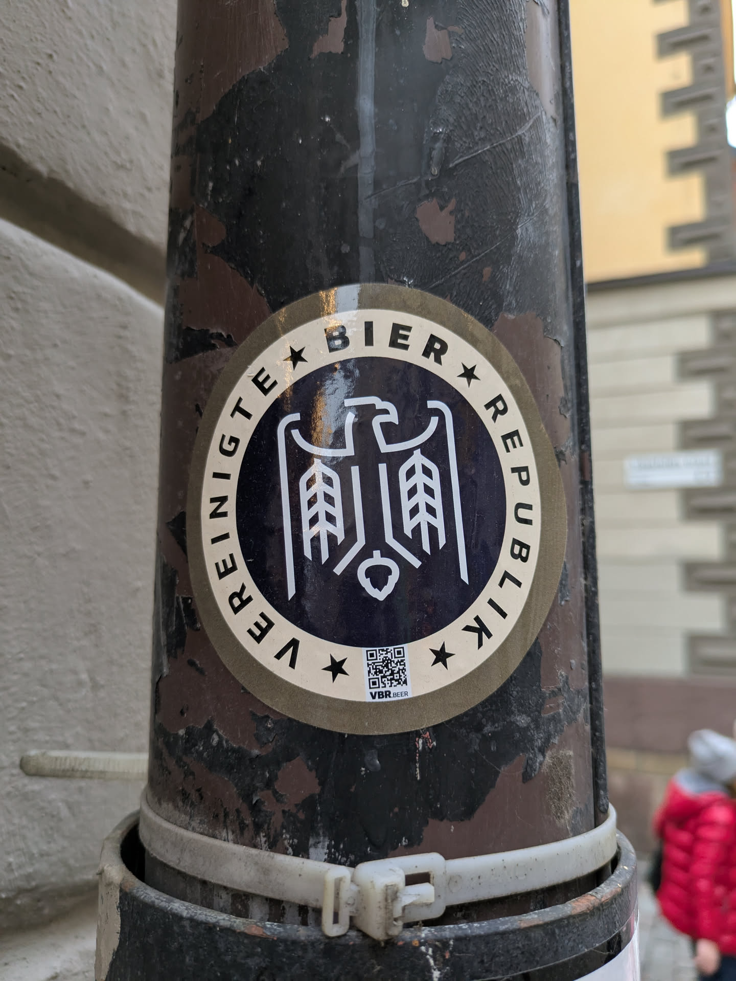 Round sticker with a dark blue center and beige outer ring. The central design features a stylized eagle with wheat stalks, and text in a circular pattern reads "Vereinigte Bier Republik" which translates to United Beer Republic. A QR code is visible at the bottom.