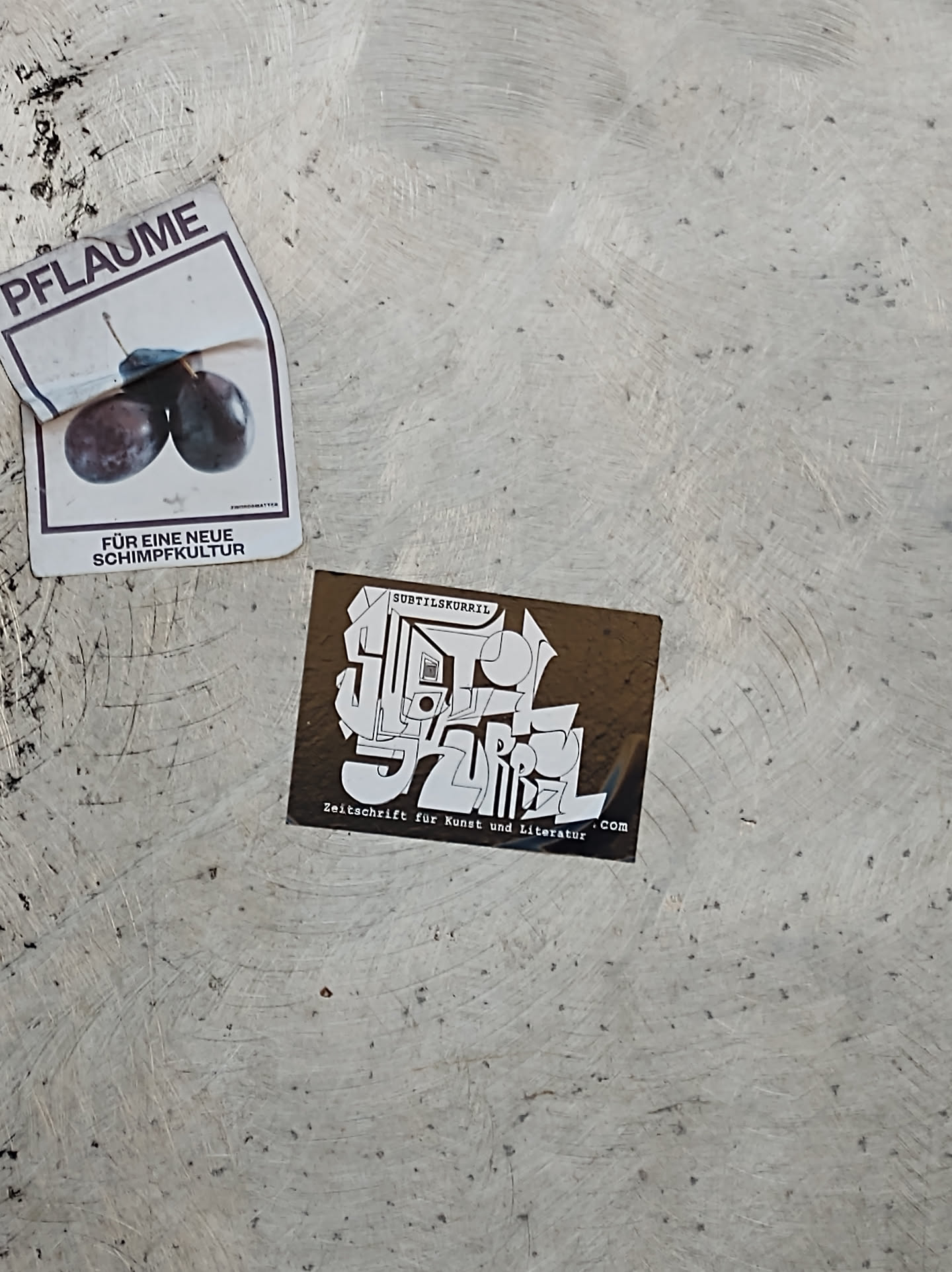 A brown square sticker with white text and graphics. The text includes the magazine's name and a tagline. The style is abstract and modern.