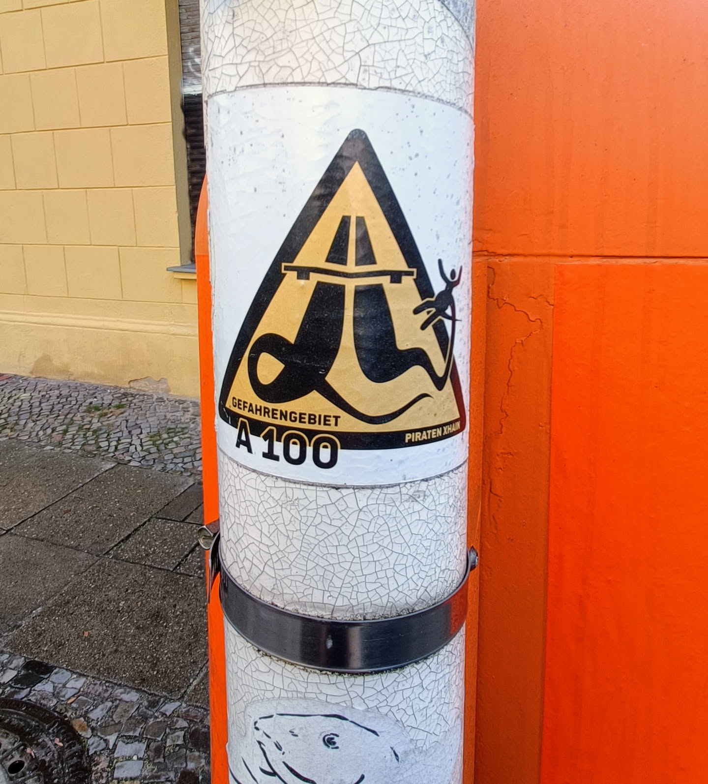 A sticker featuring a hazard warning sign with a snake-like creature on the highway. Text indicates 'Gefahrengebiet A100' (Danger Zone A100) and 'Piraten Khan'.