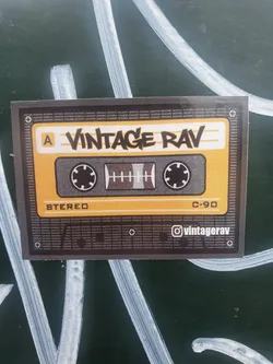 A sticker featuring a vintage cassette tape design. The text on the sticker says "Vintage Rav" and includes a social media handle @vintagerav. The cassette tape is yellow and black and says "Stereo" and "C-90".