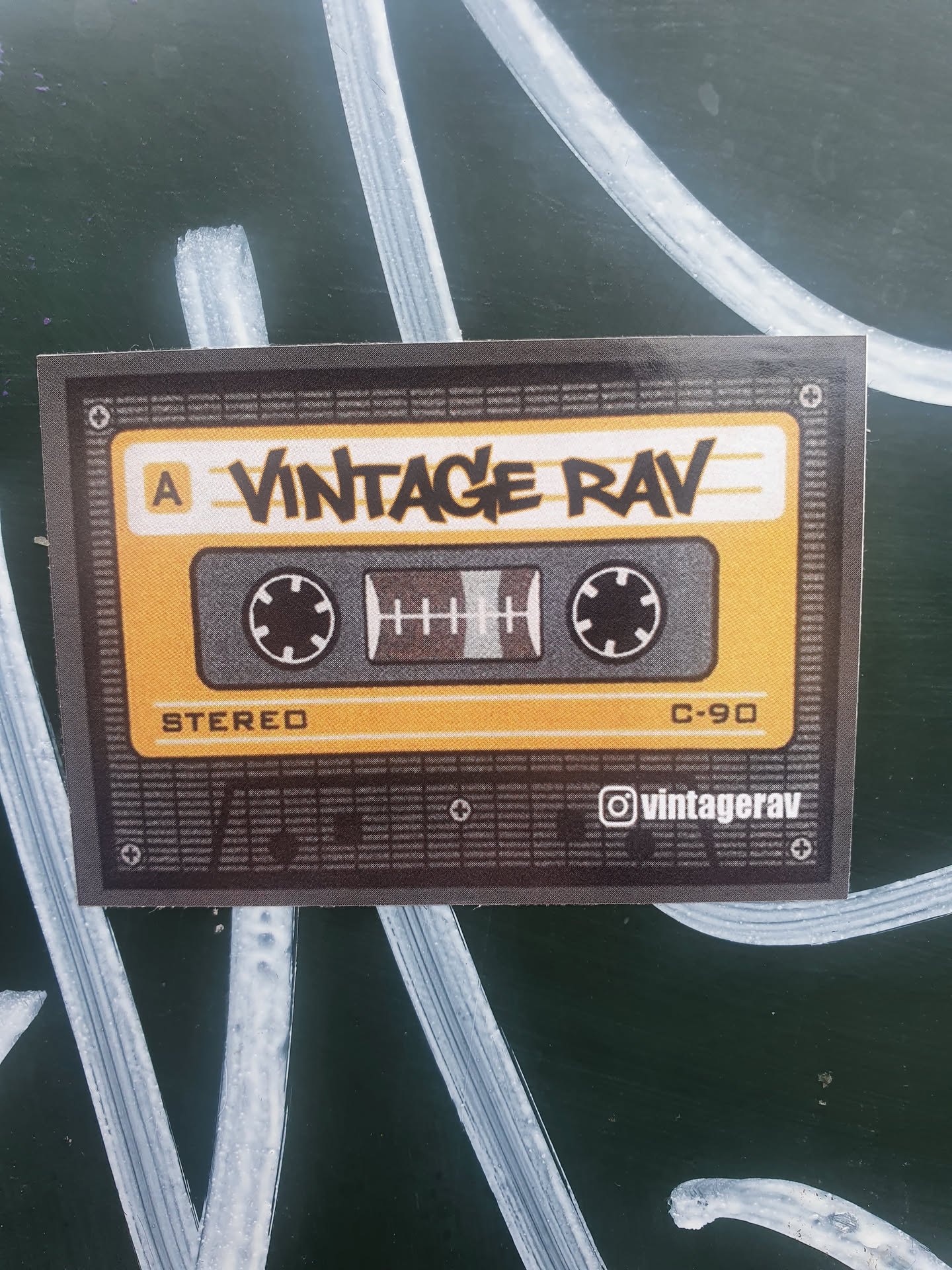 A sticker featuring a vintage cassette tape design. The text on the sticker says "Vintage Rav" and includes a social media handle @vintagerav. The cassette tape is yellow and black and says "Stereo" and "C-90".