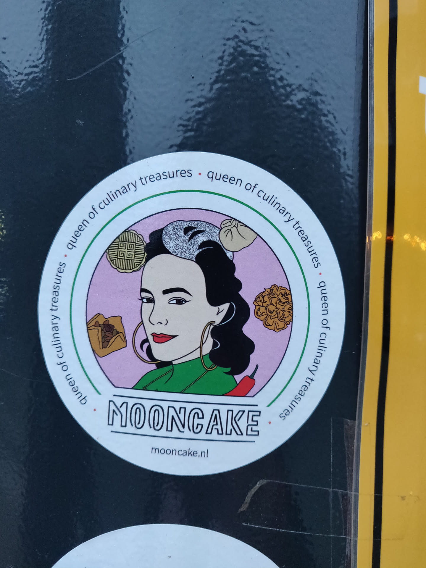 A round sticker featuring a stylized illustration of a woman with dark hair, large hoop earrings, and a green collared shirt. She is surrounded by various Asian-inspired food items such as mooncakes, dumplings and what appears to be a chili pepper. The text 'MOONCAKE' is prominently displayed below the illustration with the website mooncake.nl underneath. The phrase 'Queen of Culinary Treasures' is written around the outer edge of the sticker.