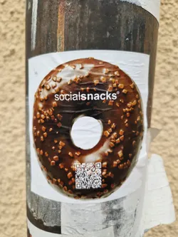 A sticker featuring a delicious-looking chocolate donut with sprinkles. The brand name "socialsnacks" is printed on the donut. A QR code is also present on the sticker.