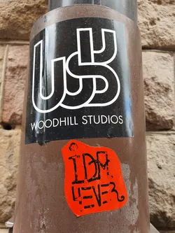 A red sticker with the text "IDM LEVE3" on top of a black sticker with the logo and name "Woodhill Studios".