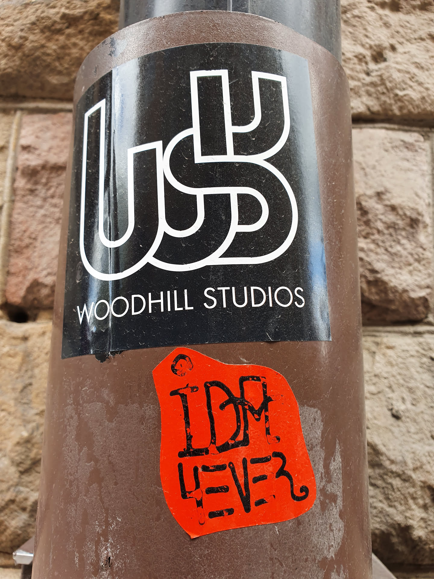 A red sticker with the text "IDM LEVE3" on top of a black sticker with the logo and name "Woodhill Studios".