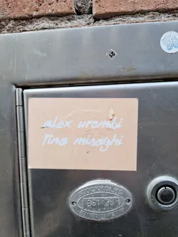 A peach-colored sticker with the names Alex Urombi and Tina Misaghi written in white. It's adhered to a metallic surface.