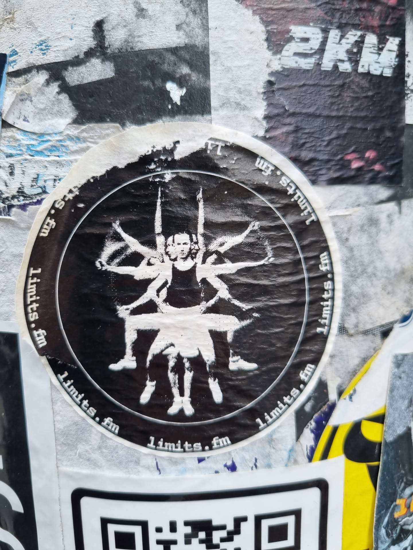A round black and white sticker with the text "limits.fm" repeating around the edge.  The central image depicts a person sitting with multiple pairs of arms reaching outward. The style is dark and slightly unsettling.