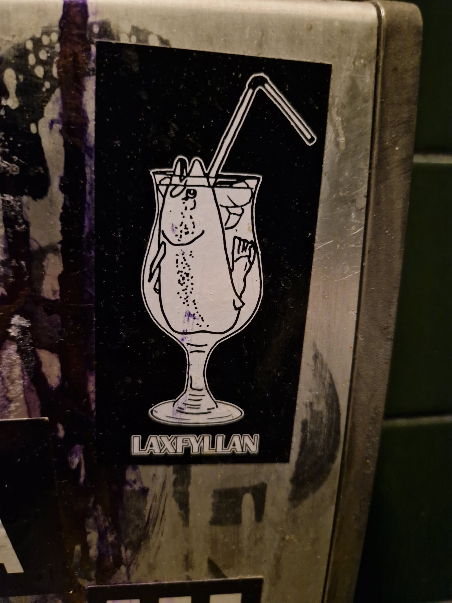 Black and white sticker of a fish in a cocktail glass with a straw. The text LAXFYLLAN is visible at the bottom.