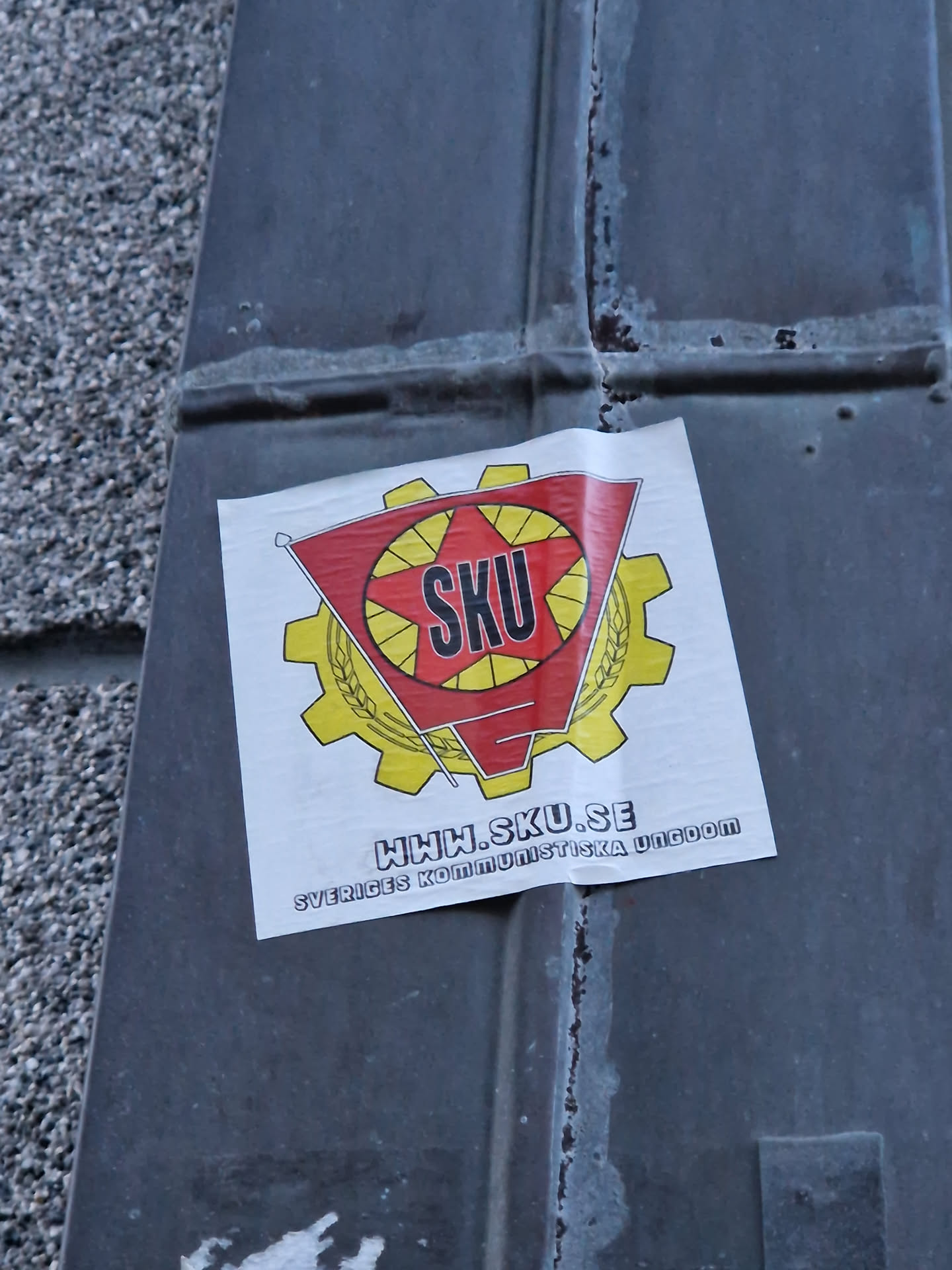 A sticker featuring the logo of Sveriges Kommunistiska Ungdom (SKU), the Swedish Communist Youth. The logo includes a red star and gear with the acronym SKU. The website www.sku.se is also displayed.