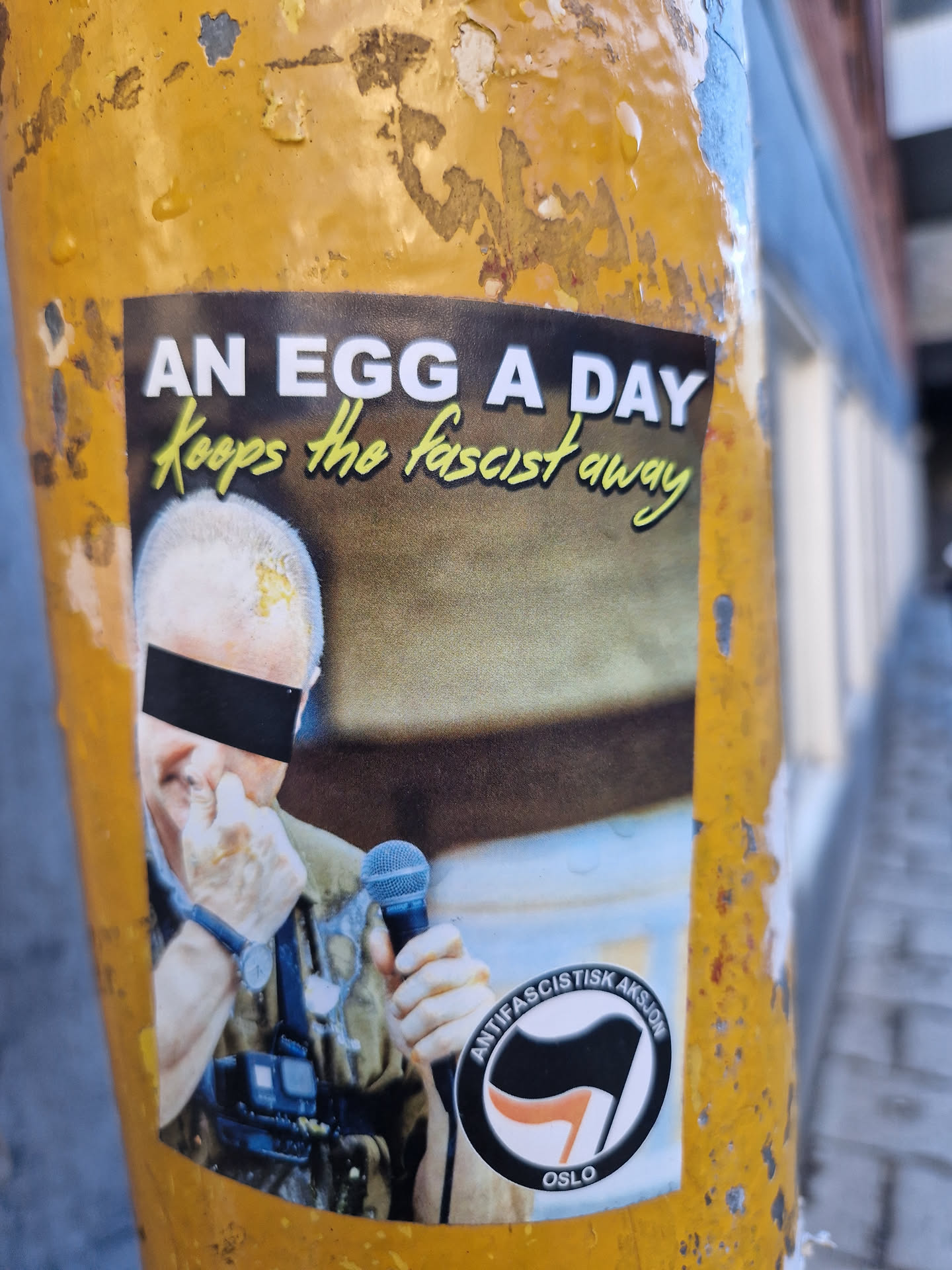 A sticker featuring a photo of a person with their face partially obscured, holding a microphone.  The text 'An egg a day keeps the fascist away' is at the top. The Anti-fascistisk aksjon Oslo logo is at the bottom.