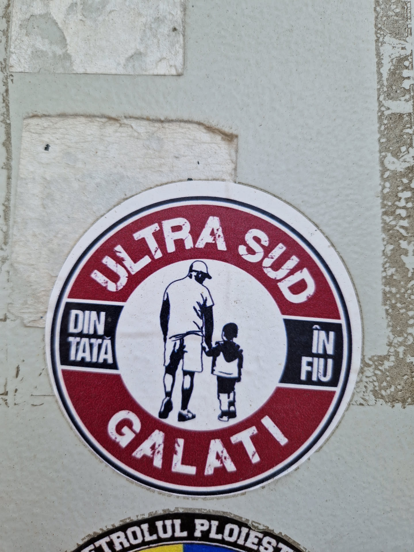 Round sticker with a red border and white center. It features a black and white illustration of a father and son holding hands. The text on the sticker says "ULTRA SUD" at the top, "DIN TATA" on the left, "ÎN FIU" on the right, and "GALATI" at the bottom.