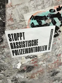 A sticker with the text "STOPPT RASSISTISCHE POLIZEIKONTROLLEN" (Stop racist police checks) in German.  The sticker also includes a website address: wrangelkiez.united-blogs.org
