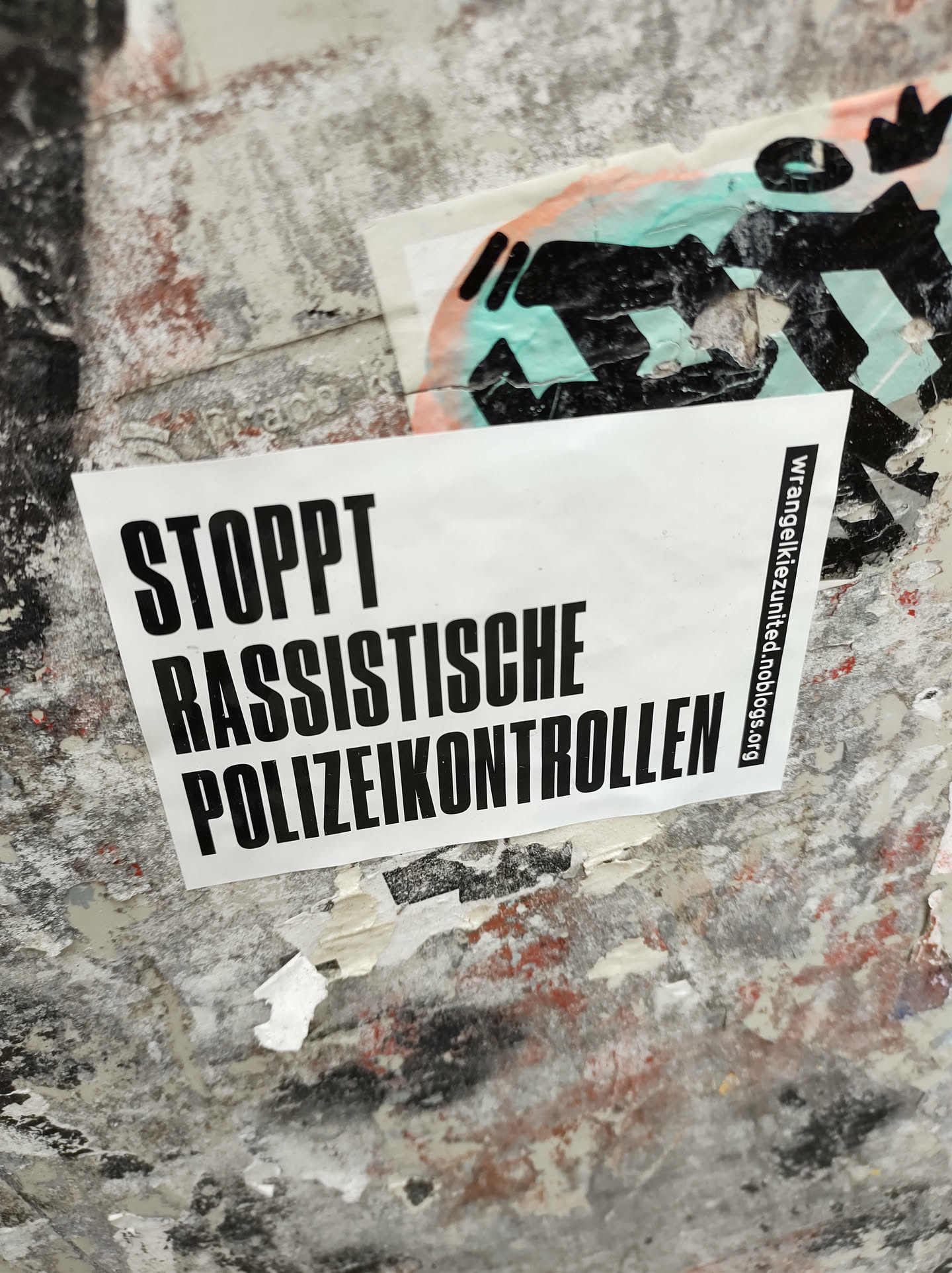A sticker with the text "STOPPT RASSISTISCHE POLIZEIKONTROLLEN" (Stop racist police checks) in German.  The sticker also includes a website address: wrangelkiez.united-blogs.org