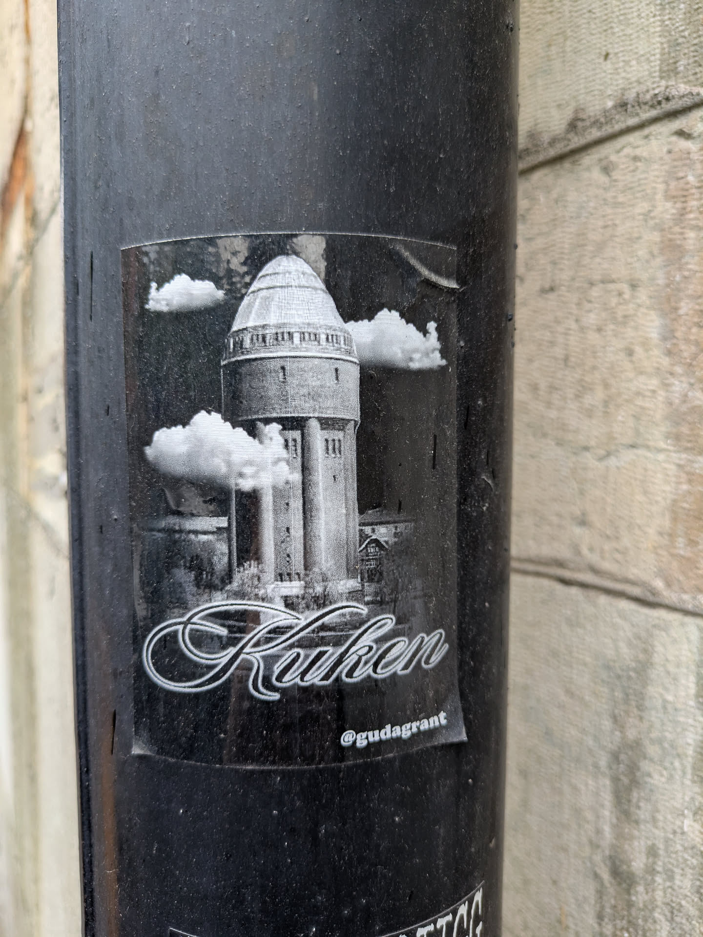 This black and white sticker shows a water tower surrounded by clouds, with the word "Kuken" below in a calligraphic font. It also includes the Instagram handle @gudagrant.
