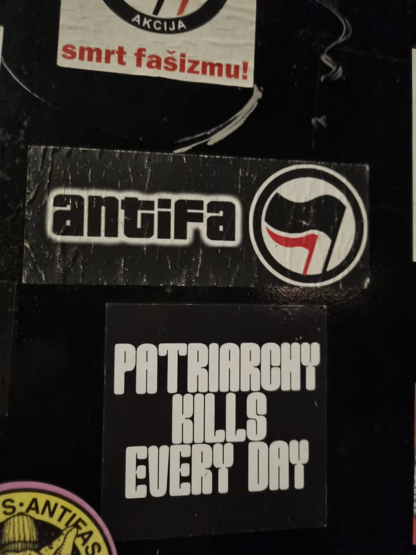 A black and white sticker with the text "Patriarchy Kills Every Day" in bold, uppercase letters.  There is a smaller Antifa sticker above it, featuring the Antifa symbol.