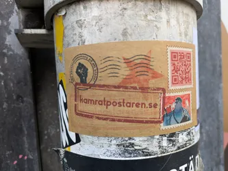 A sticker featuring the KamratPosten website address, a QR code, and various stamps. The aesthetic is reminiscent of vintage postal stamps with a rebellious twist. The main text reads 'kamratposten.se'.