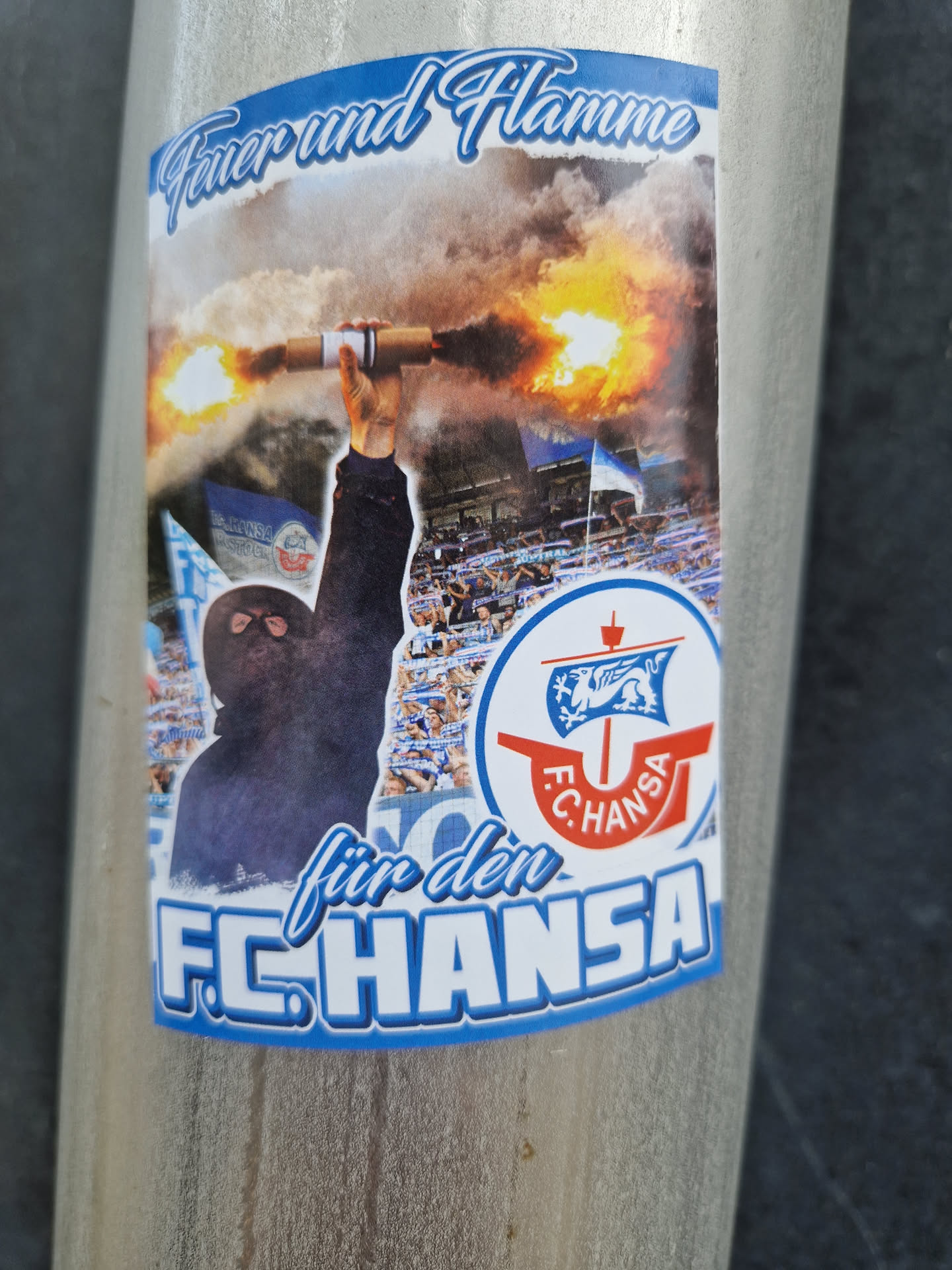 A sticker depicting a person holding a burning flare in a stadium with a crowd of people. The sticker features the logo of FC Hansa Rostock and the text "Feuer und Flamme für den FC Hansa", which translates to "Fire and flame for FC Hansa".