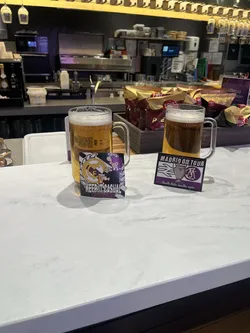 A rectangular sticker with a slightly curved bottom edge, featuring a stylized character wearing a purple beanie and a striped purple and white scarf, holding a beer mug. The iconic Real Madrid C.F. crest, in gold and purple, is visible behind the character. Bold, pixelated white text reads 'KEEP IT CASUAL' above smaller text 'CASUALS MADRID'. The design uses a palette of purple, gold, white, and black, reflecting a football fan or casuals subculture aesthetic.